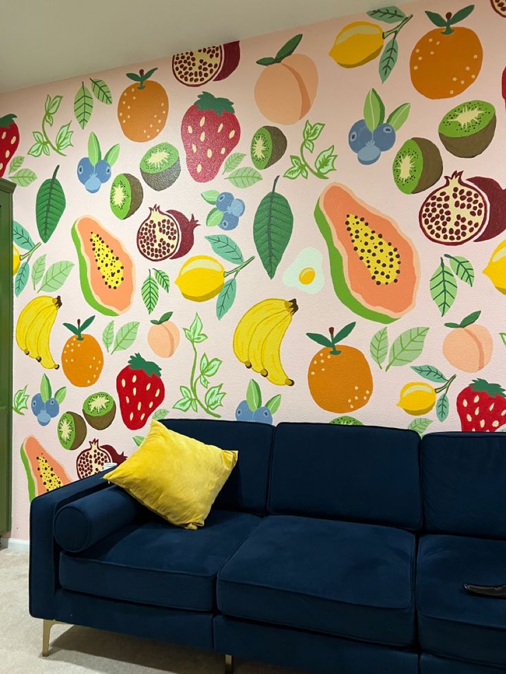 a blue couch sitting in front of a wall with fruit painted on it's walls