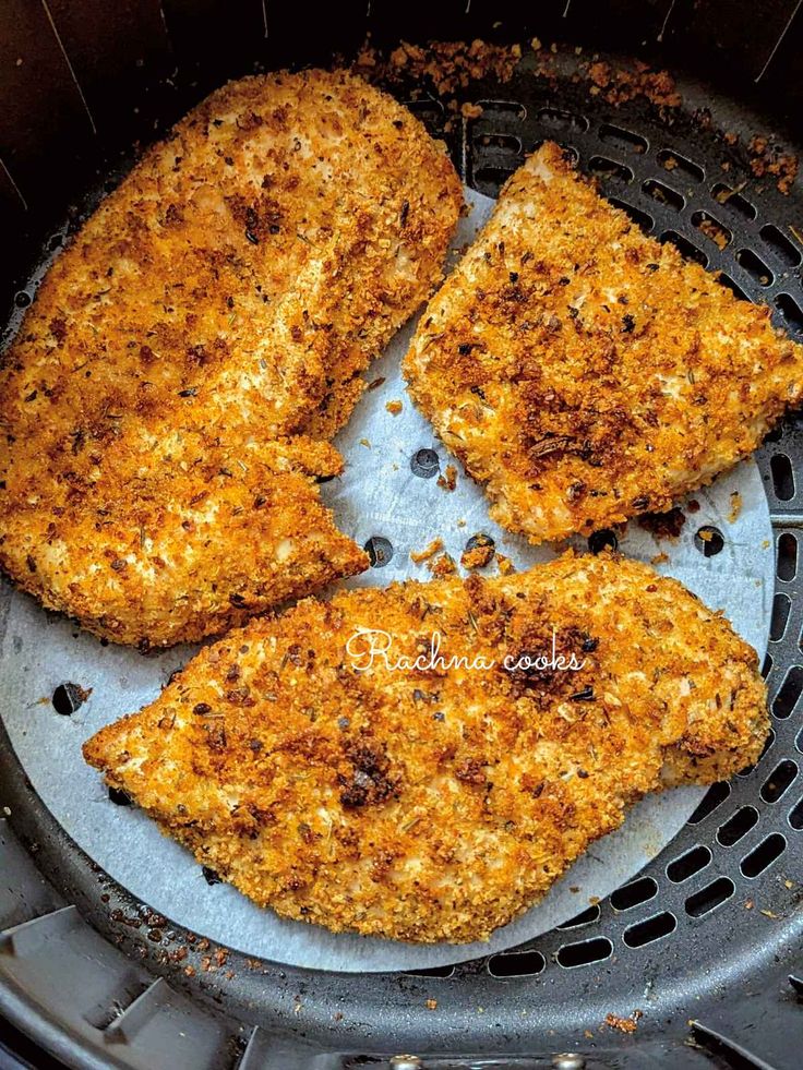 four pieces of chicken sitting in an air fryer pan with the bottom half covered