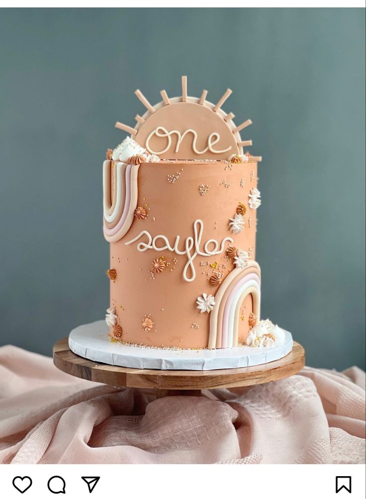 a pink and white cake with the words one joy written on it is sitting on a wooden platter