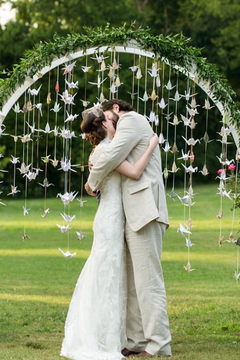 a bride and groom kissing in front of a wedding arch with paper cranes hanging from it