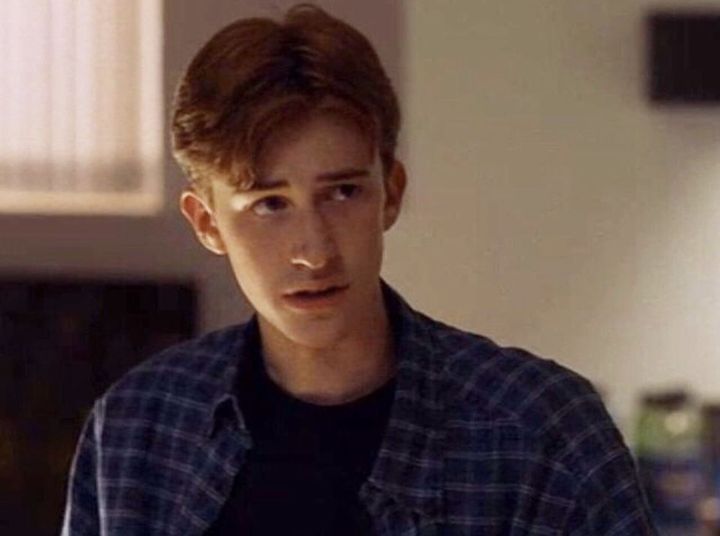 a young man with red hair wearing a blue and white checkered shirt looking at the camera