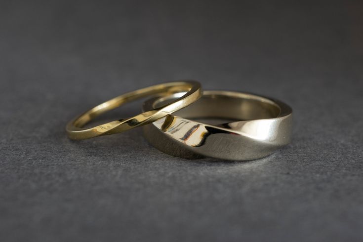 two gold wedding rings sitting side by side on top of a gray surface with one ring in the middle