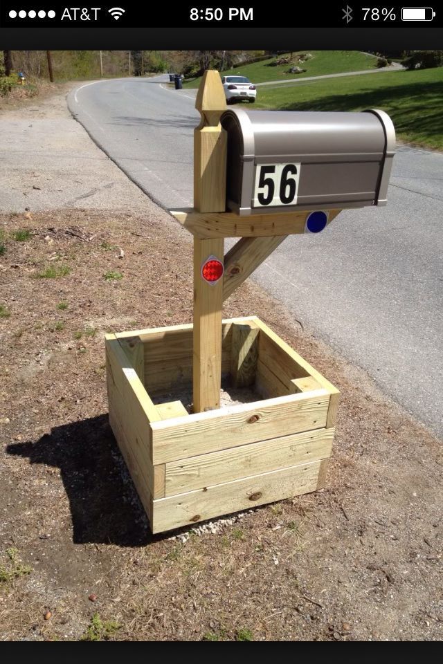 a mailbox sitting on the side of a road next to a wooden planter