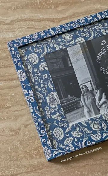 an old blue and white photo frame on a wooden table with a flowered pattern