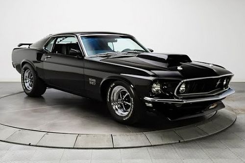 a black muscle car is on display in a room with white walls and flooring