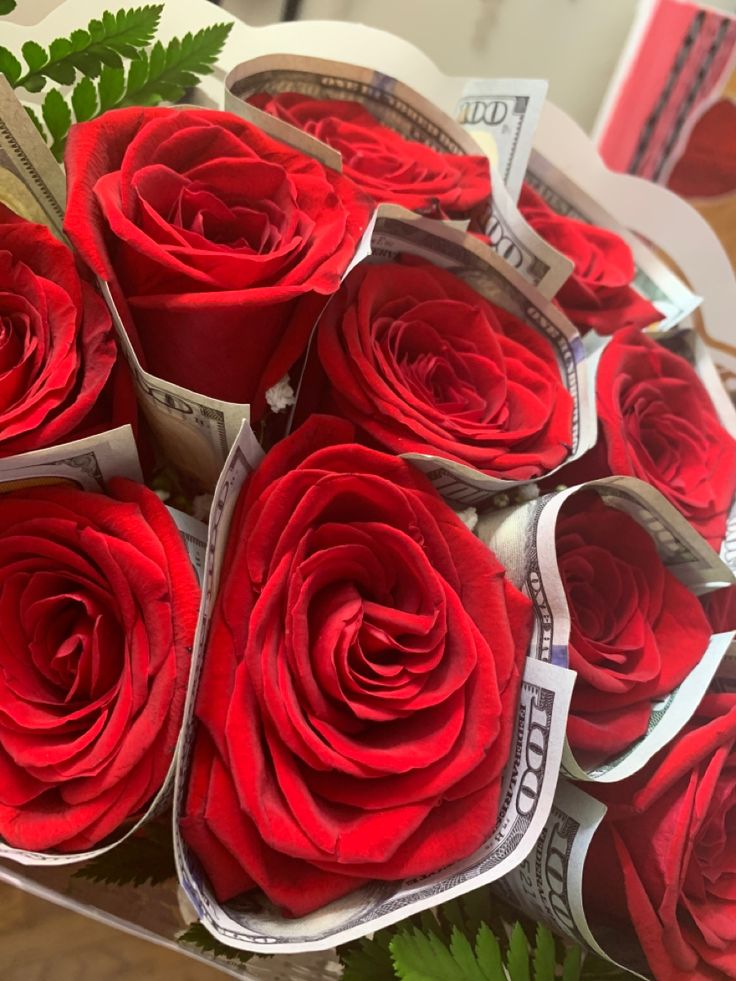 a bouquet of red roses sitting on top of a table next to some money bills