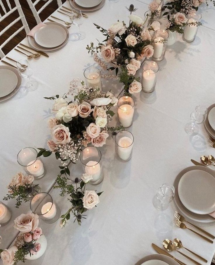 a long table is set with white and pink flowers, candles, and silverware