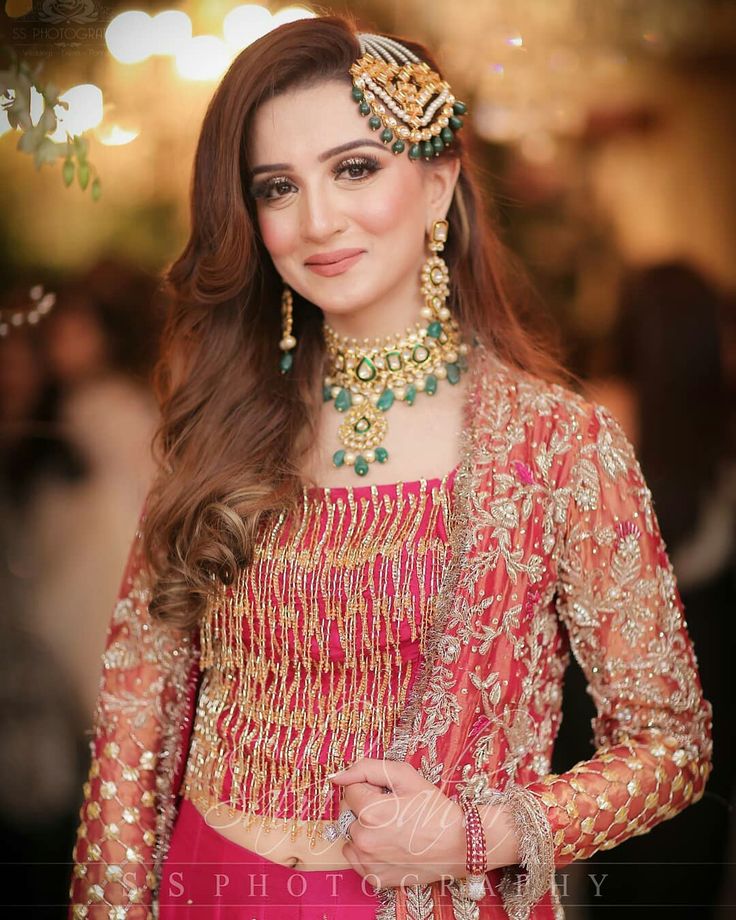 a woman in a red and gold lehenga with jewelry on her head, smiling at the camera