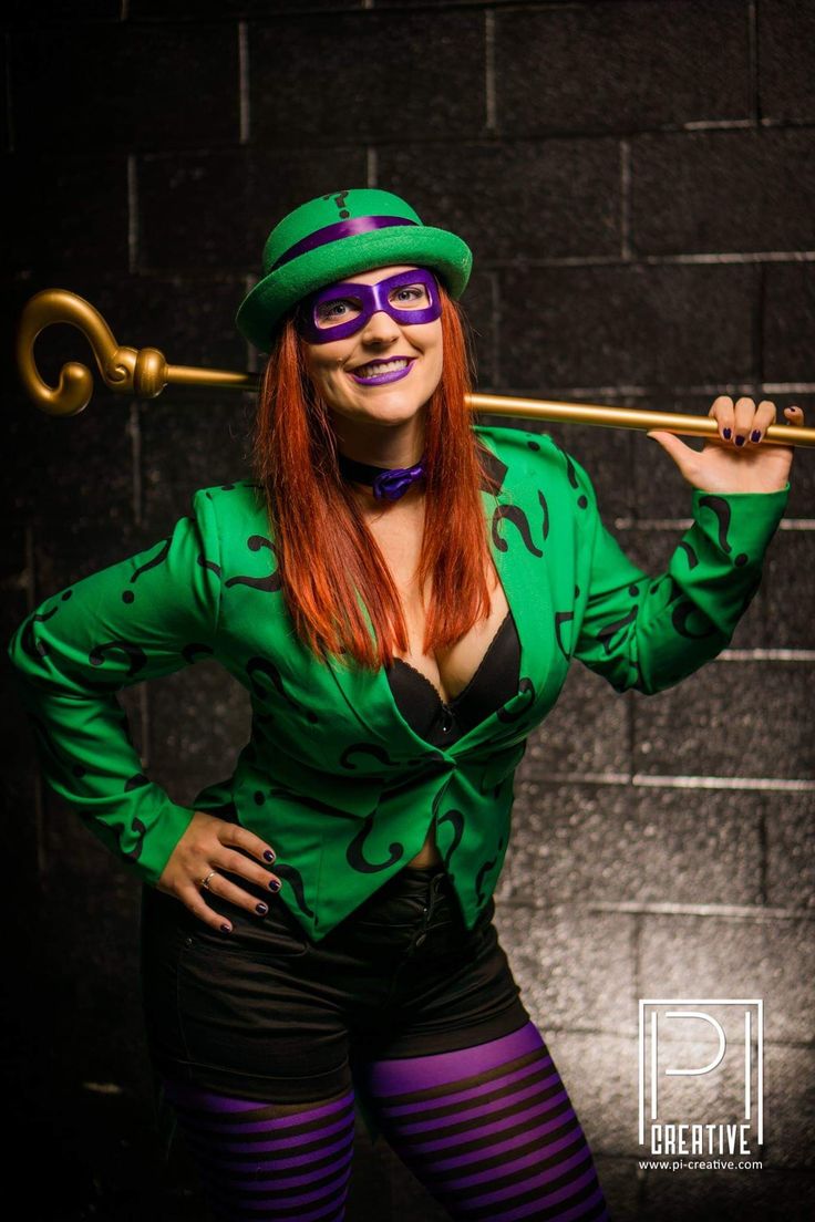 a woman dressed in green and purple poses for the camera while holding a stick with her right hand