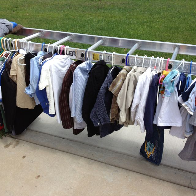 clothes are hanging on the rail in front of a grassy area with a man standing next to it