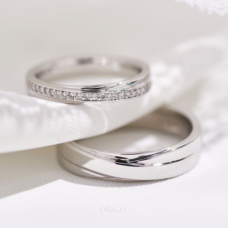 two wedding rings sitting on top of each other next to a white cloth covered pillow