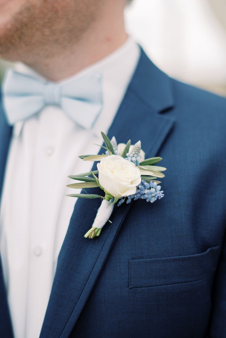 a man wearing a blue suit and bow tie with a white flower on his lapel