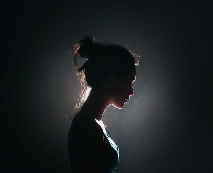 a woman standing in the dark with her head turned to the side and light shining on her face