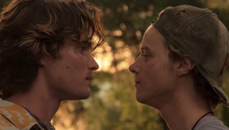 two young men standing next to each other in front of the sun, with trees behind them