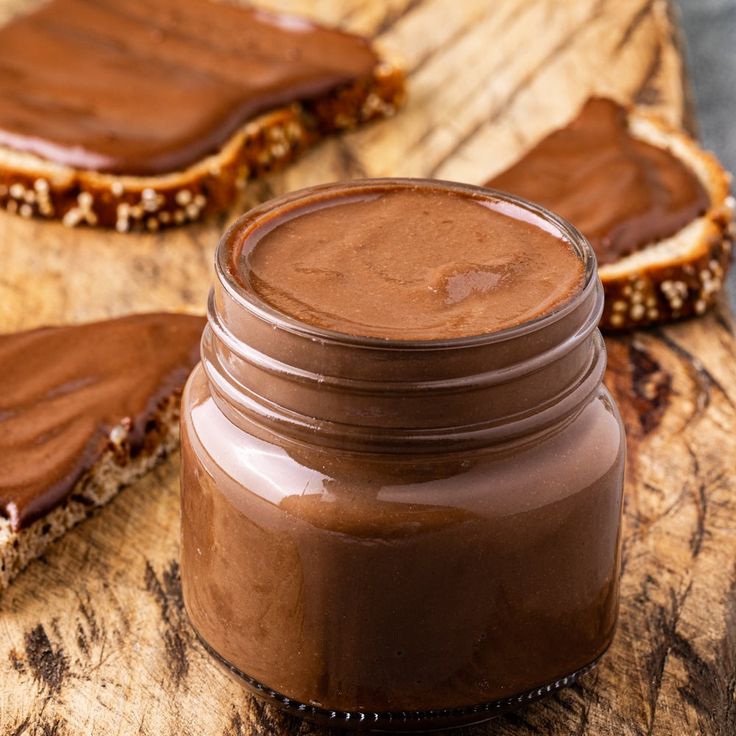 peanut butter spread in a jar next to two pieces of bread on a cutting board