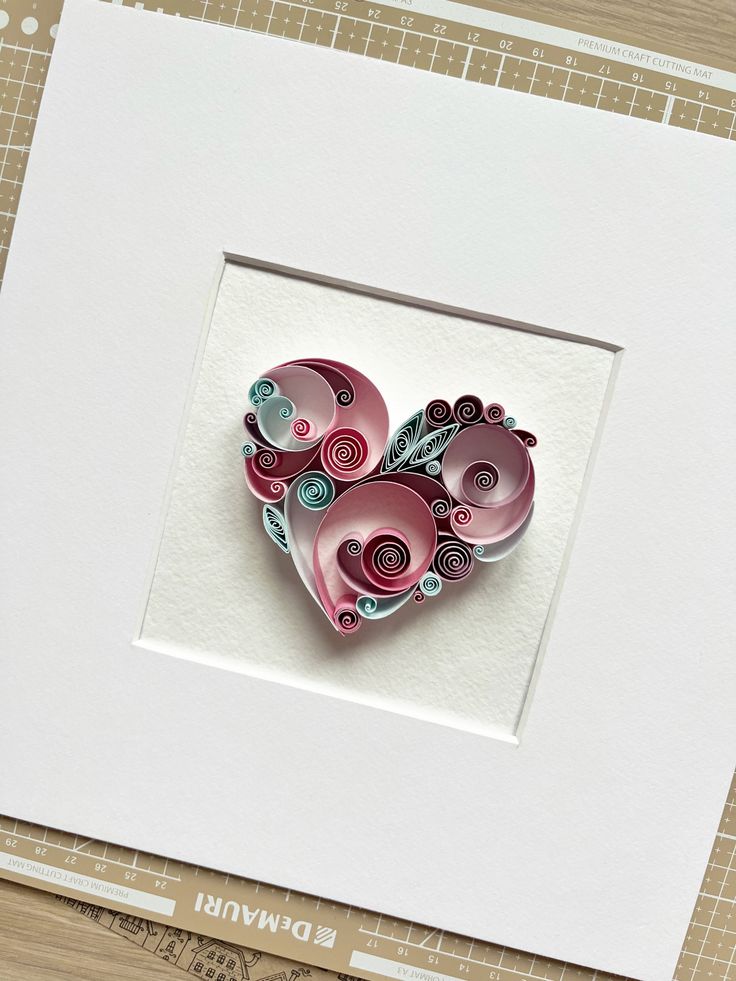 a heart shaped brooch sitting on top of a piece of paper in a white frame