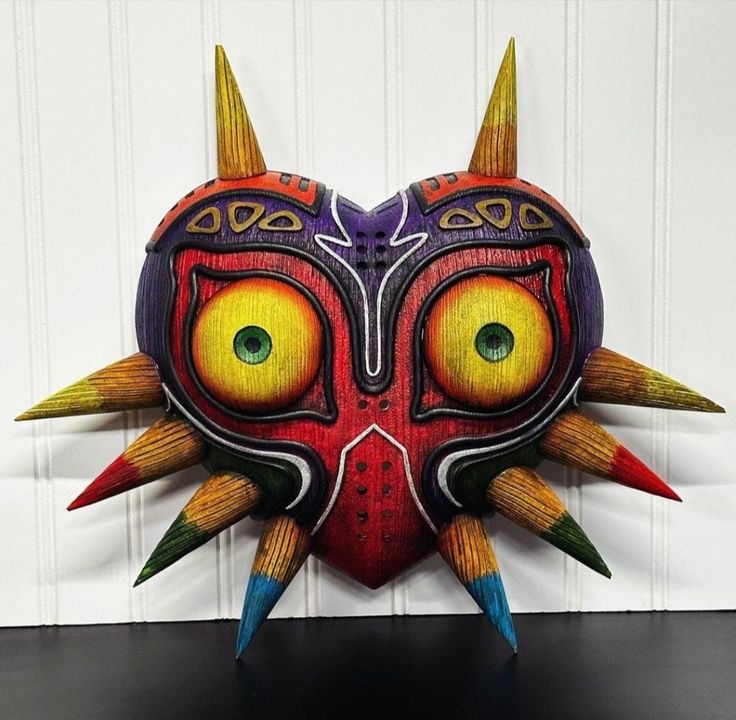 a colorful mask with horns and spikes on it's face is hanging from the wall