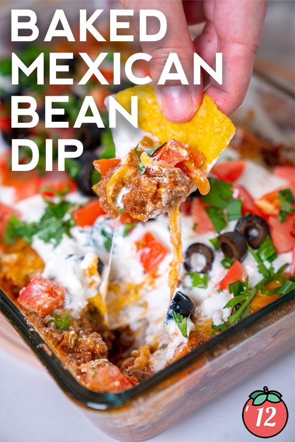 a hand dipping a tortilla chip into a casserole dish filled with mexican bean dip