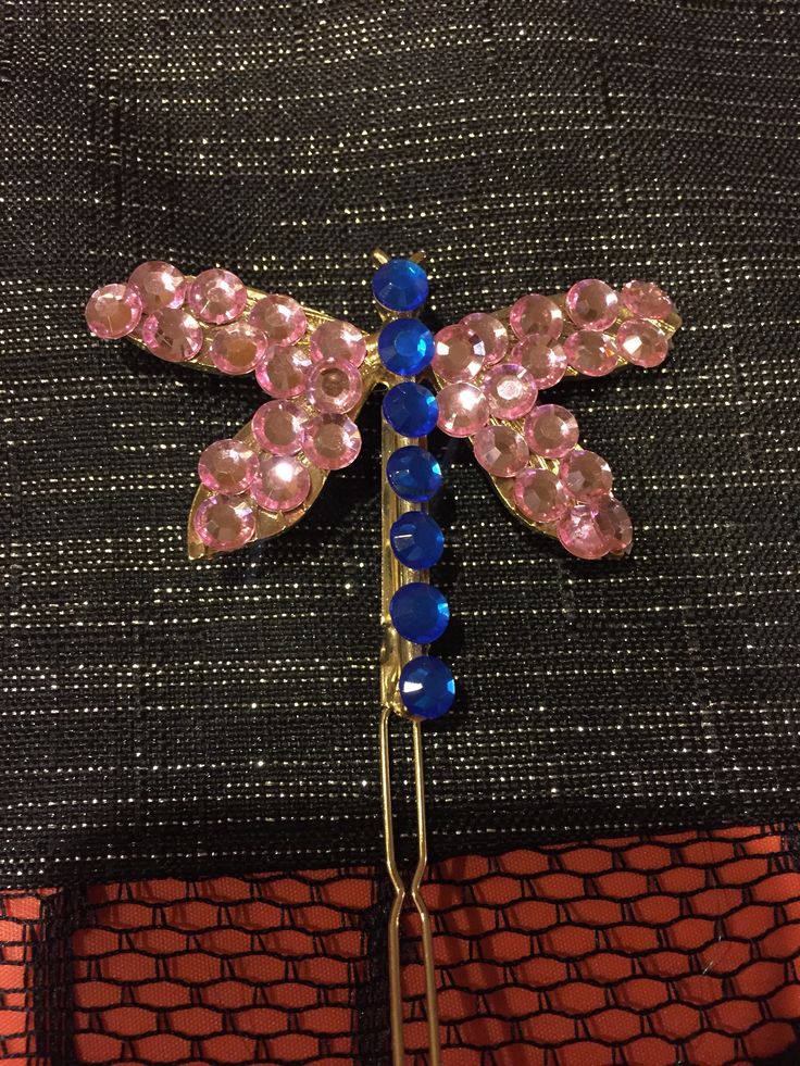 a pink and blue dragonfly brooch sitting on top of a piece of cloth