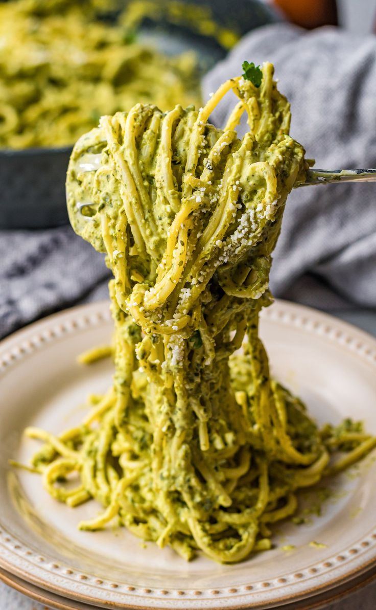 a fork full of pesto pasta on a plate with another dish in the background