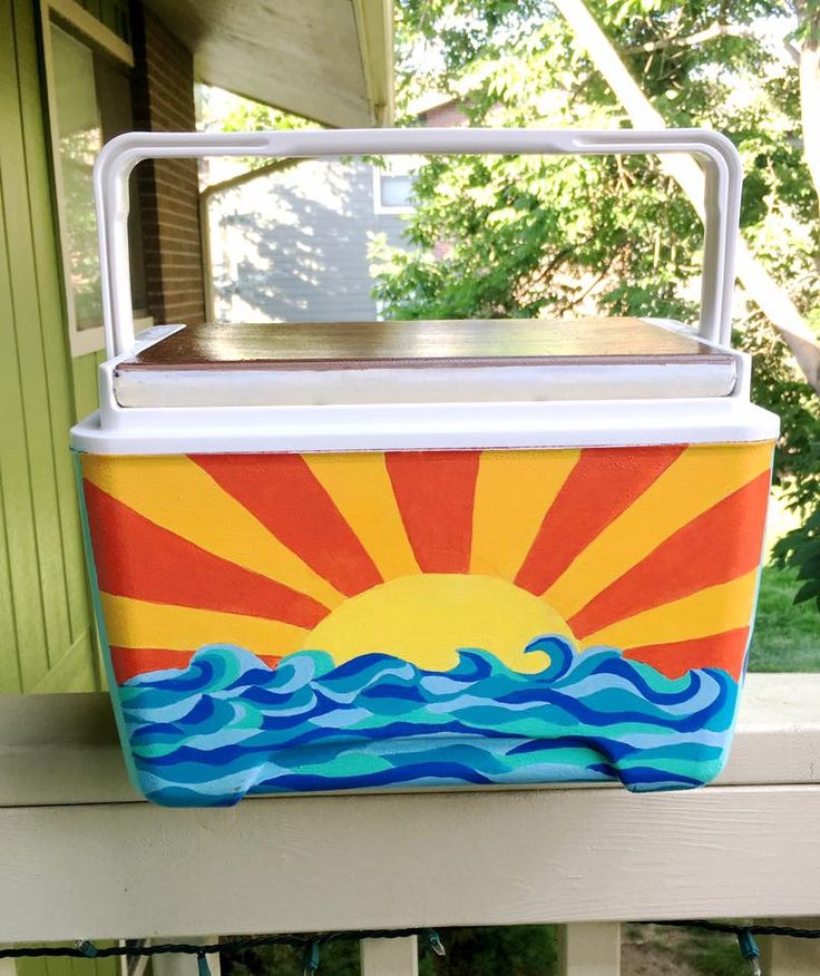 a cooler with the sun painted on it sitting on a porch next to a tree