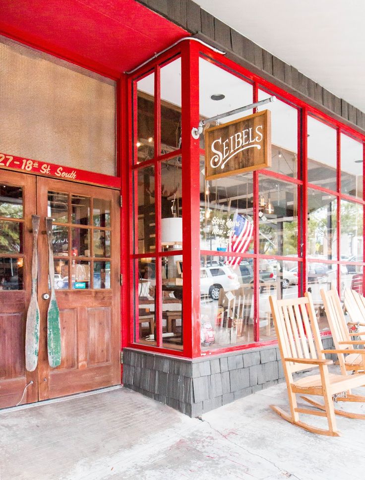 two rocking chairs sitting in front of a red storefront with glass doors and windows