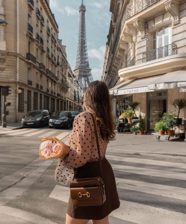 a woman is walking down the street with a bag and donut in her hand