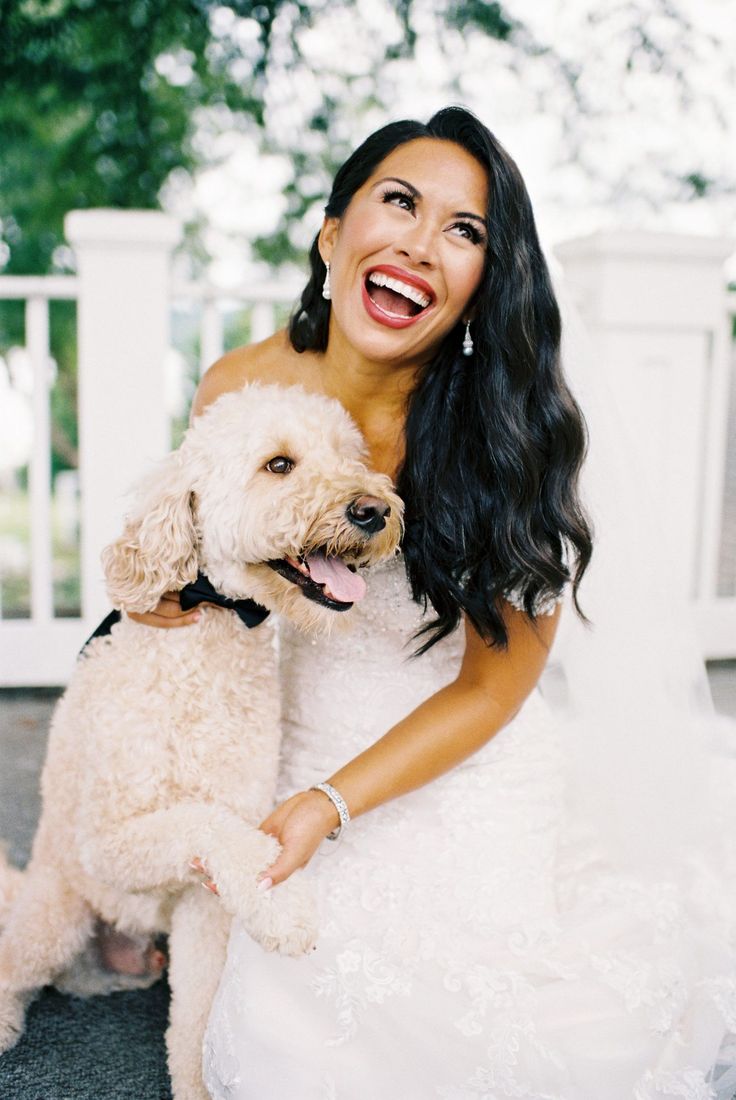 a woman in a wedding dress is holding a white dog and smiling at the camera