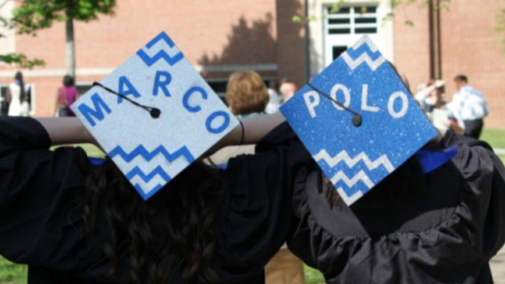 two graduates in caps and gowns hold their hats over their heads