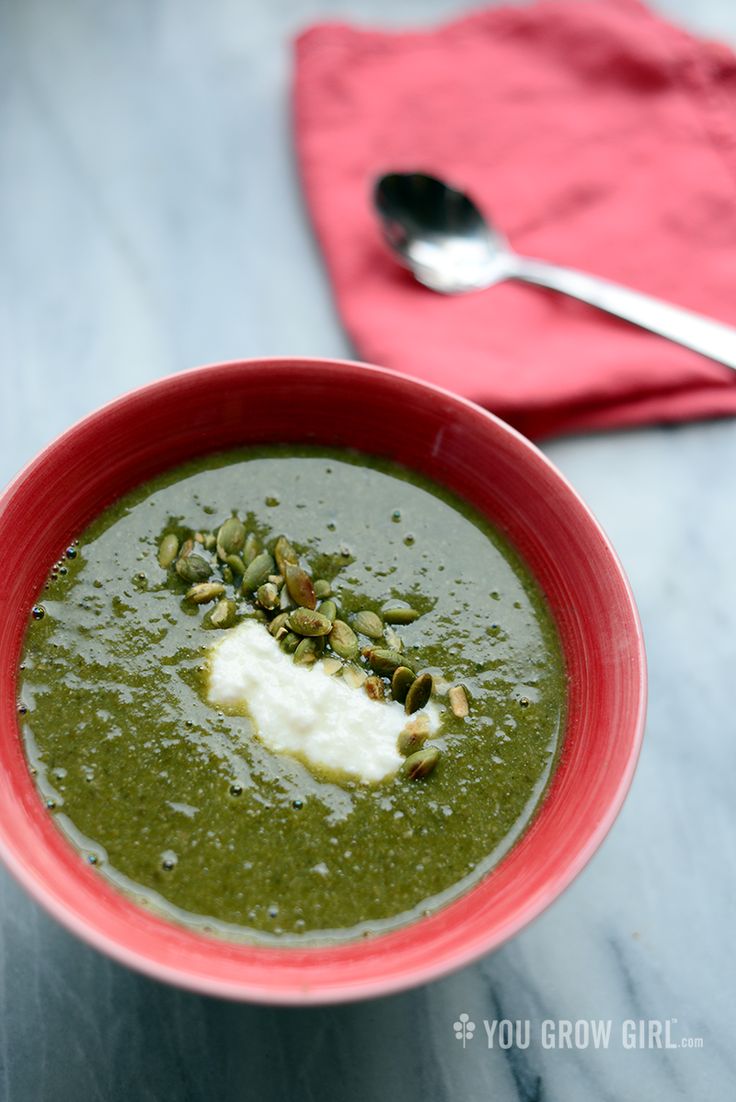 a red bowl filled with green soup on top of a table next to a spoon