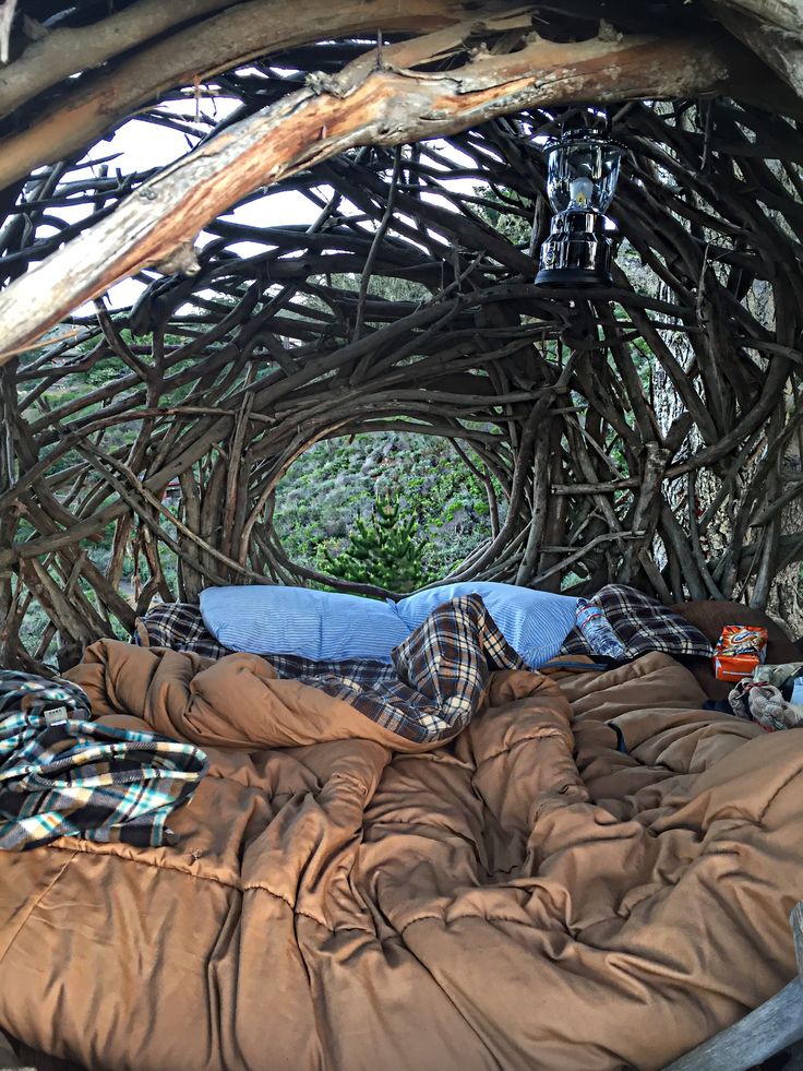 an image of a bed made out of branches and blankets in the woods with a sleeping bag on top