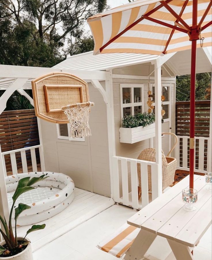 a small white house with an orange and white striped umbrella over the porch, next to a picnic table