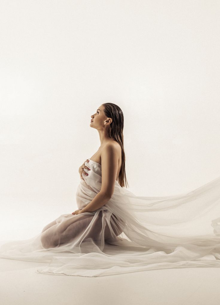 a pregnant woman sitting on the floor with her veil flying in the air over her head