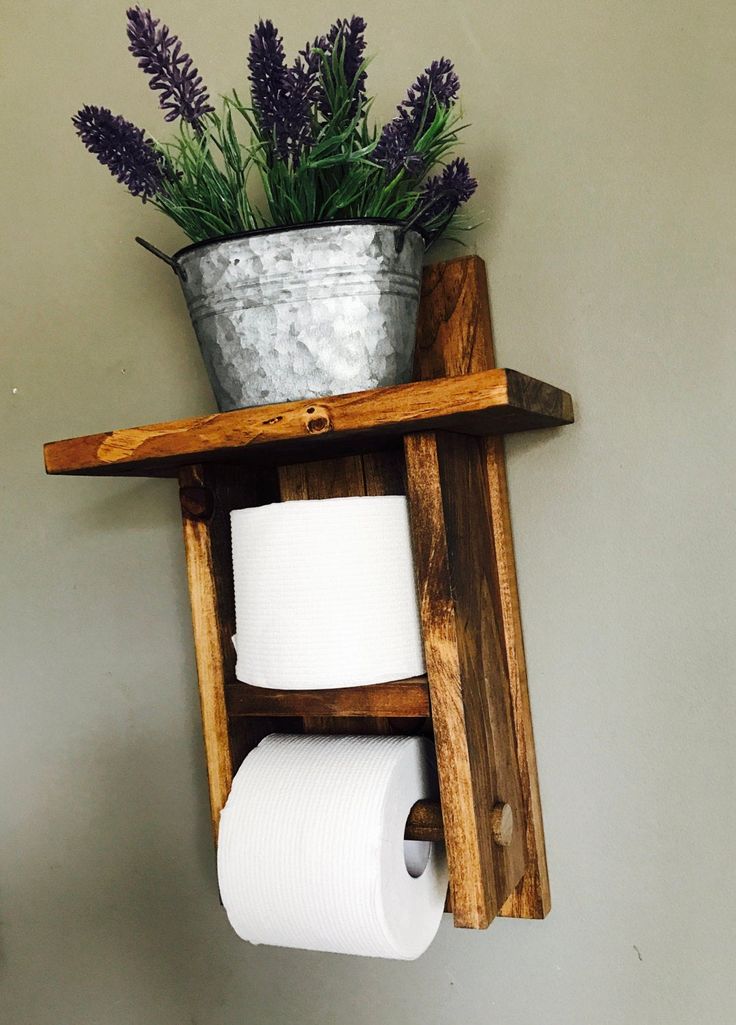 a wooden shelf holding two rolls of toilet paper and a potted plant on top