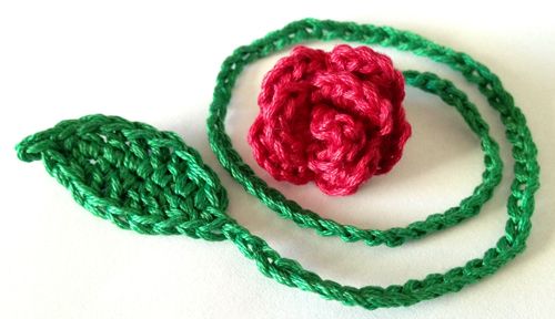 a crocheted rose is sitting on a green lanyard with a red flower