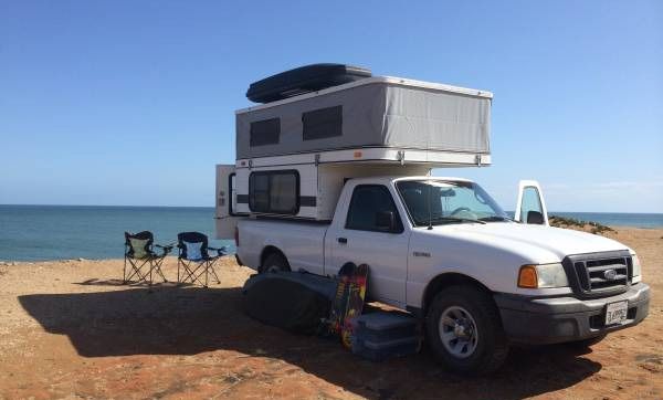 a truck with a camper attached to it parked on the beach near the ocean