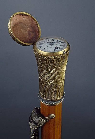 a gold and white clock sitting on top of a wooden pole next to a metal object