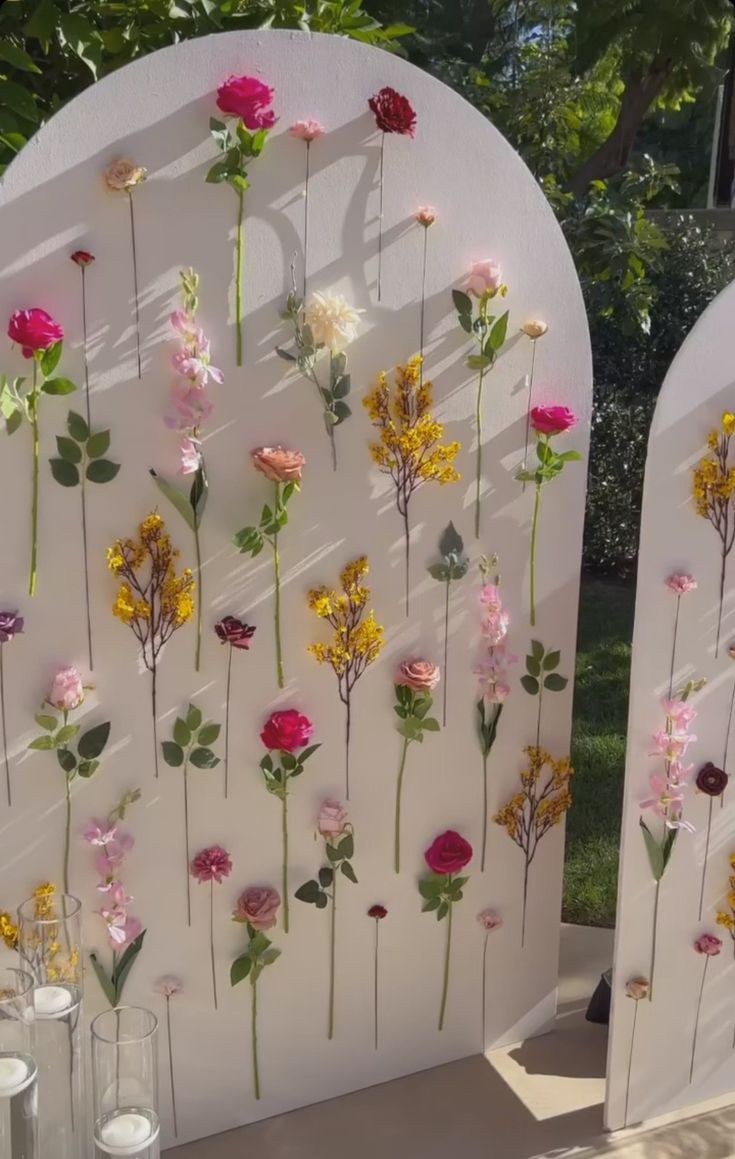 several flowers are arranged on the side of a white arch that is decorated with glass vases and candles