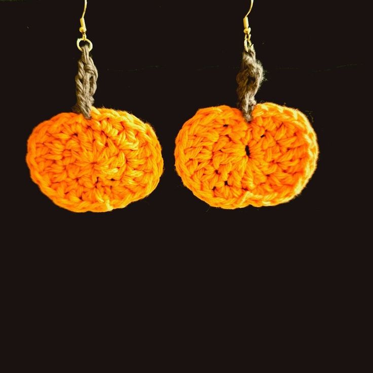 two orange crocheted pumpkins hanging from hooks on a black background, one is yellow and the other is orange