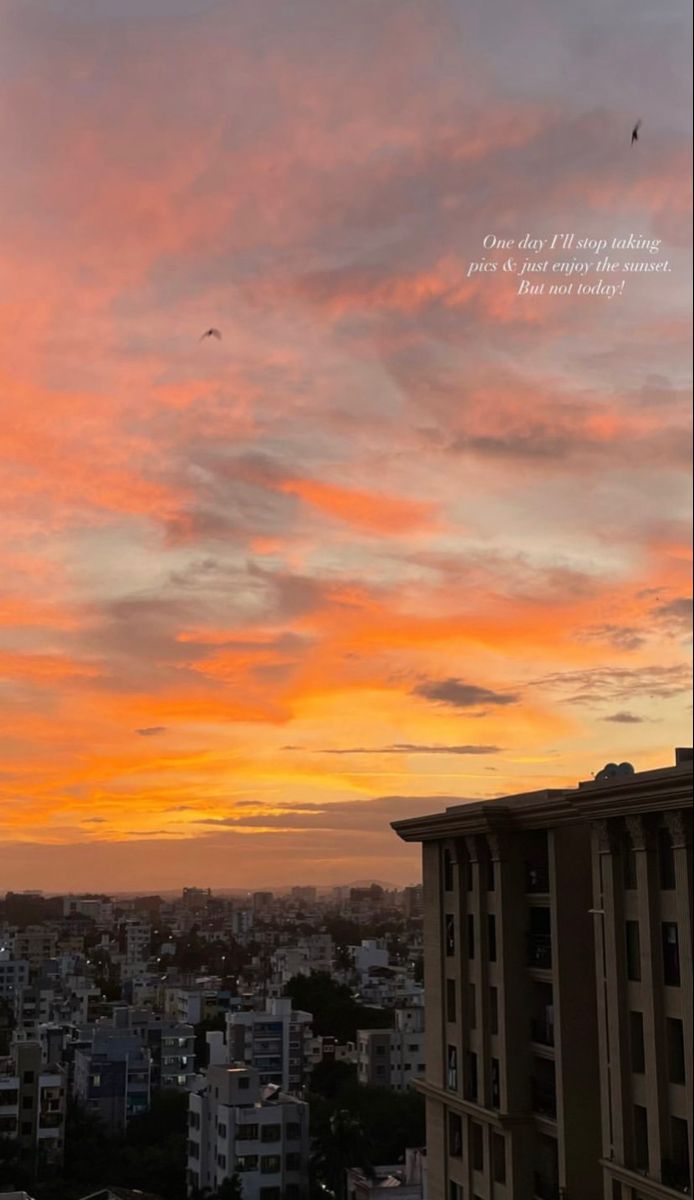 an orange and pink sky with buildings in the background