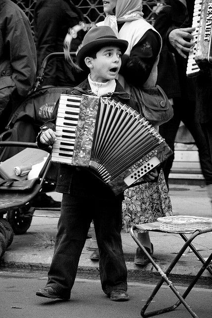 a young boy is playing an accordion in front of some other people on the street