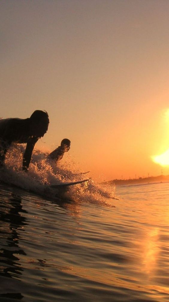 two people on surfboards in the water at sunset