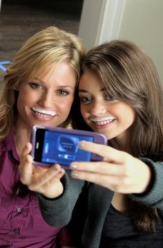 two women are taking a selfie with their cell phone in front of the camera