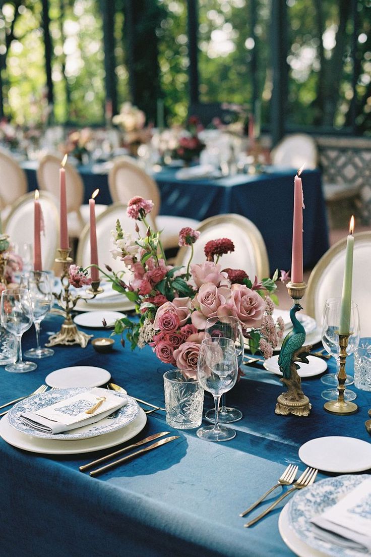 the table is set with blue linens and white plates, silverware, and pink flowers