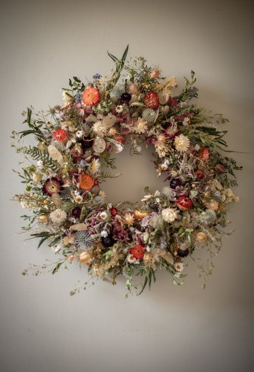 a wreath hanging on the wall with dried flowers and greenery around it's edges