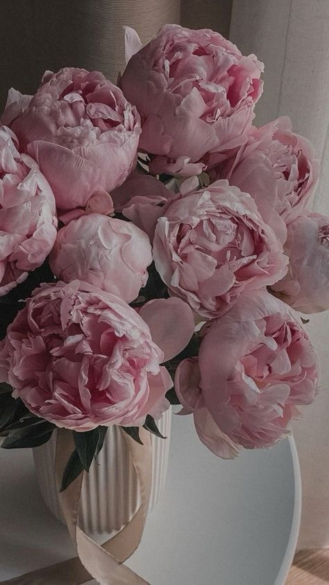 a bouquet of pink peonies in a white vase on a window sill