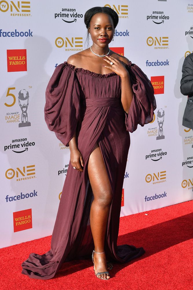 a woman in a purple dress and hat on the red carpet at an awards event