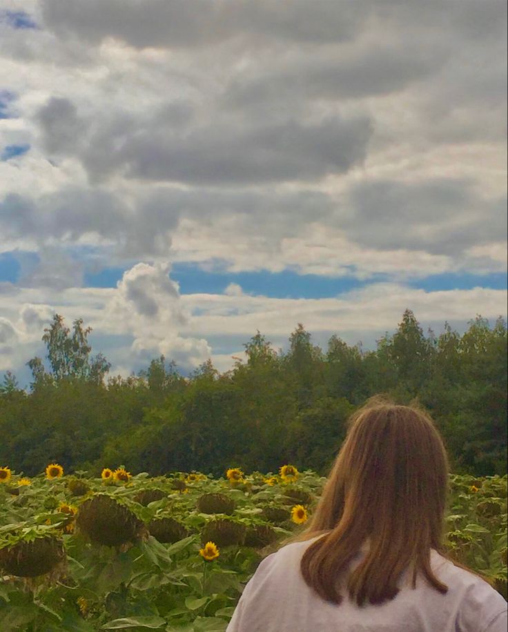 a woman standing in front of a field of sunflowers with clouds above her