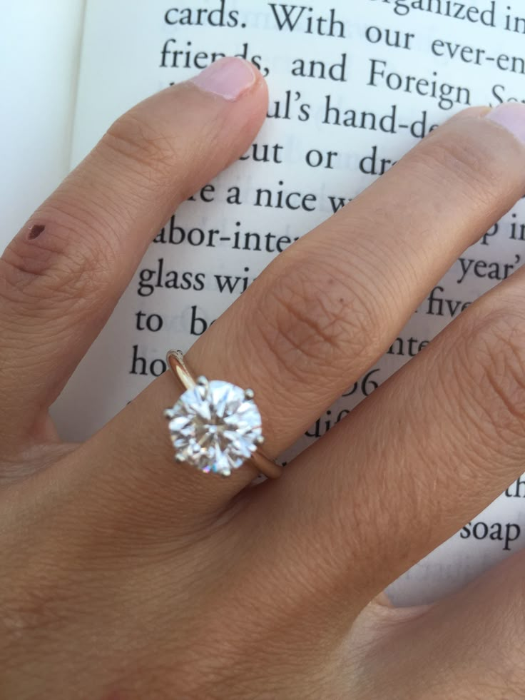 a close up of a person's hand with a ring on top of an open book