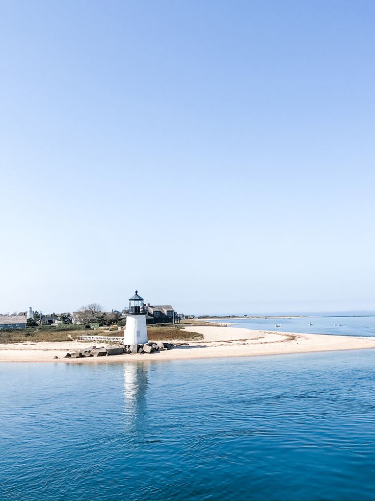 an island with a light house in the middle of it and blue water around it